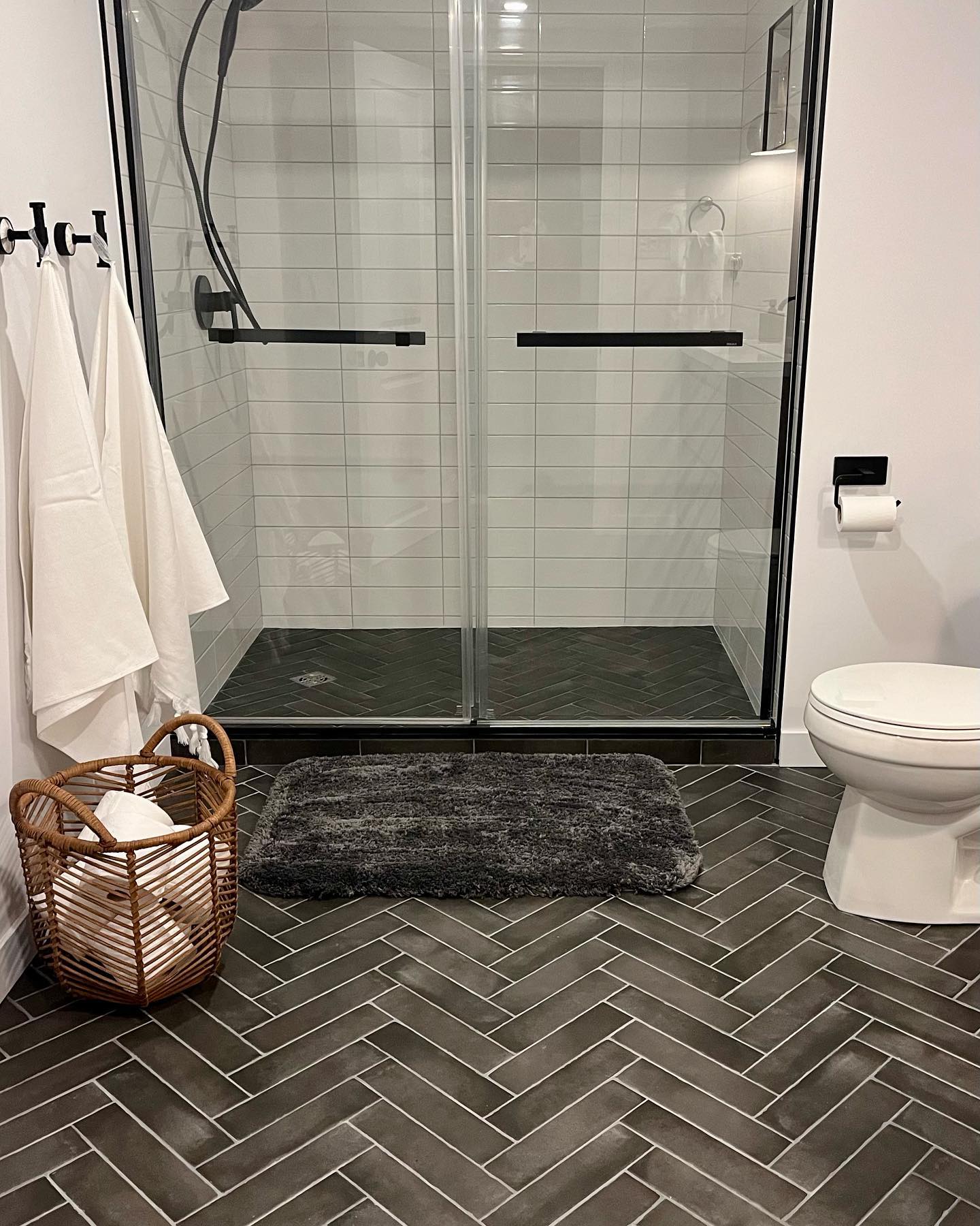 Finished basement bathroom with dark gray herringbone tile floor and black framed glass shower