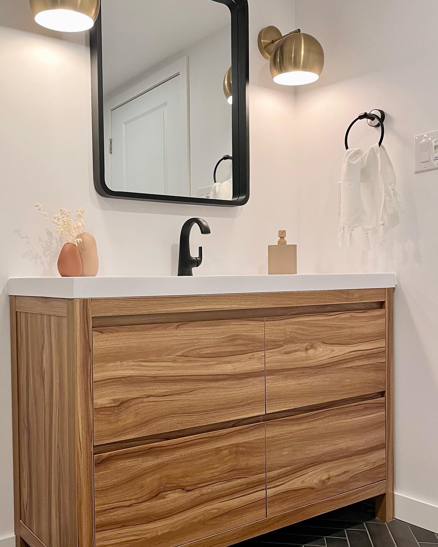 Close view of herringbone floor tile meeting the wood vanity and black framed mirror