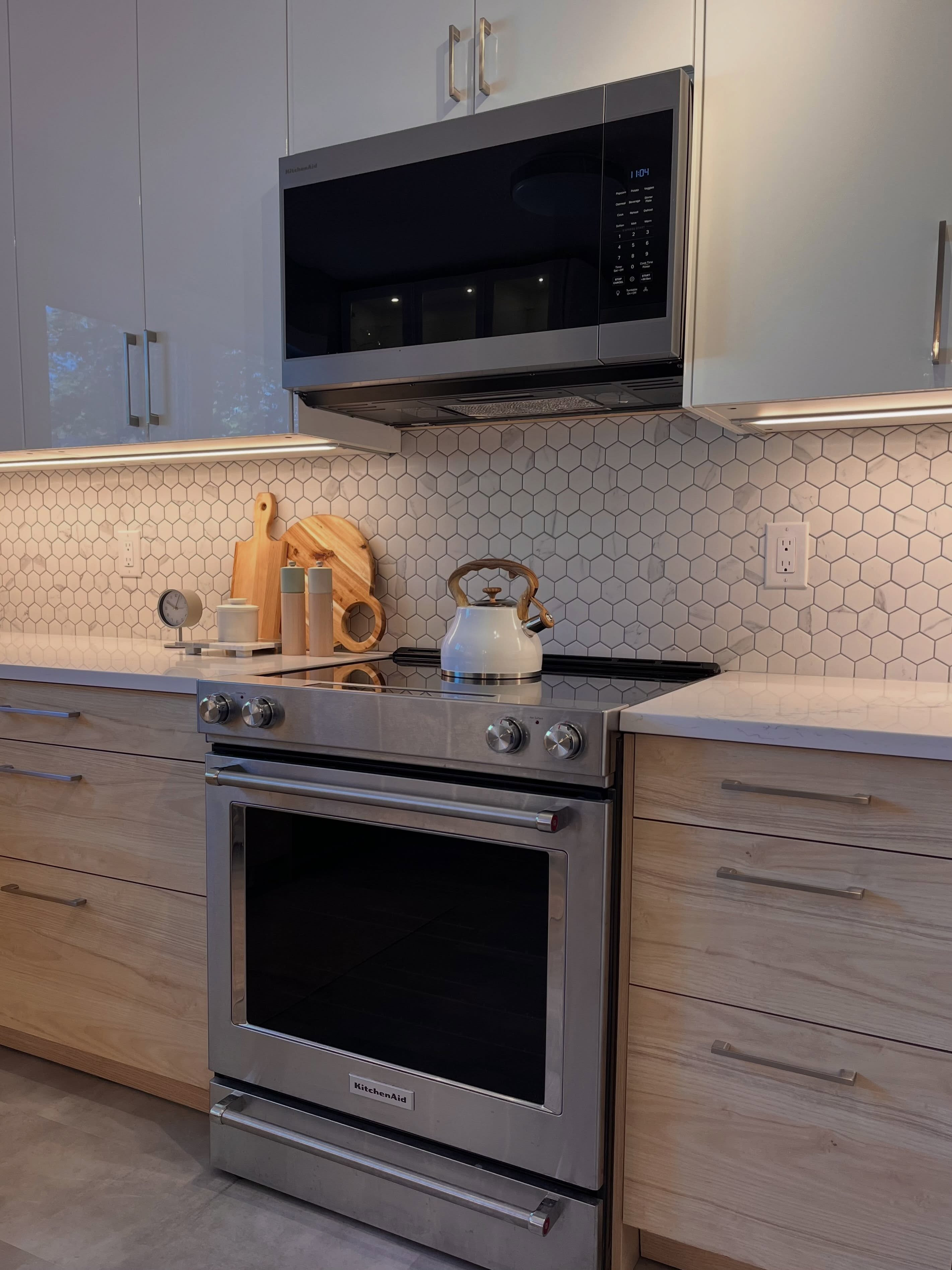 Finished Winnipeg IKEA kitchen with white upper cabinets, wood lower cabinets, hexagon marble tile, and a stainless range