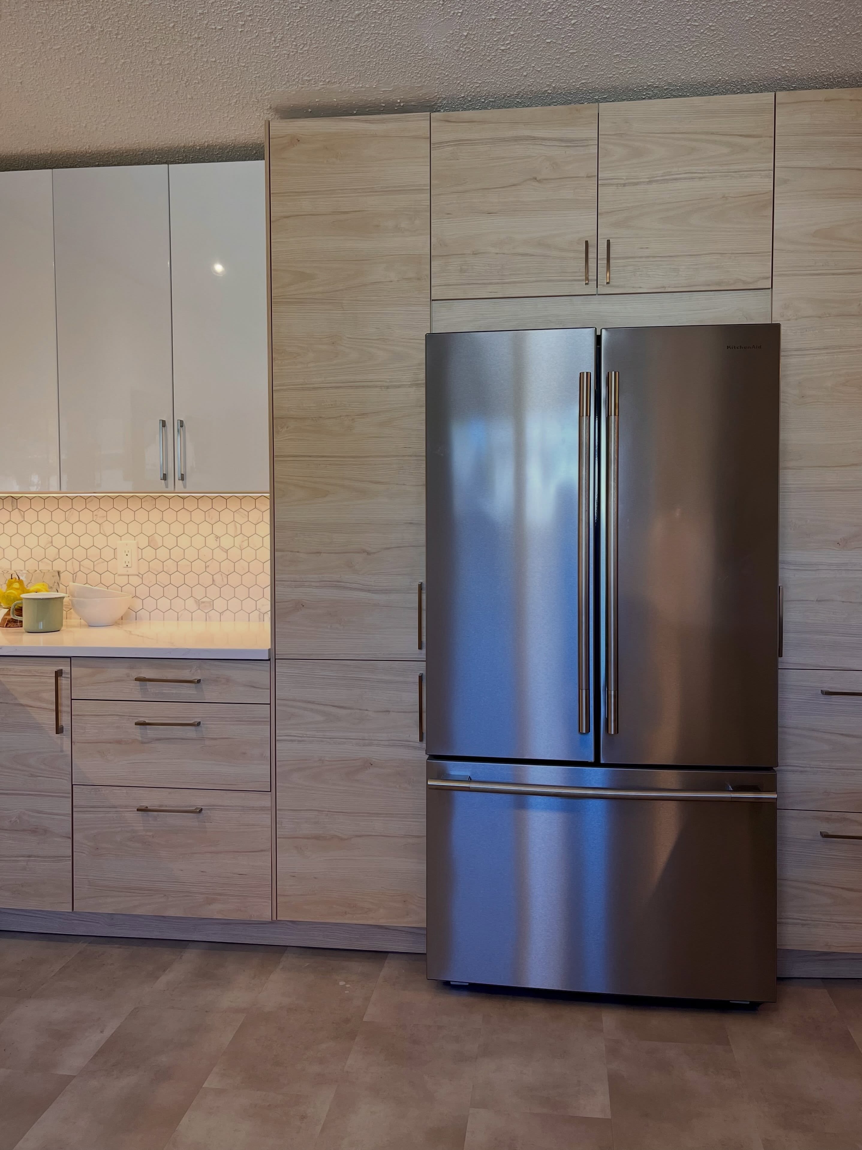 Finished Winnipeg kitchen refrigerator wall with tall white cabinets and warm wood base cabinets