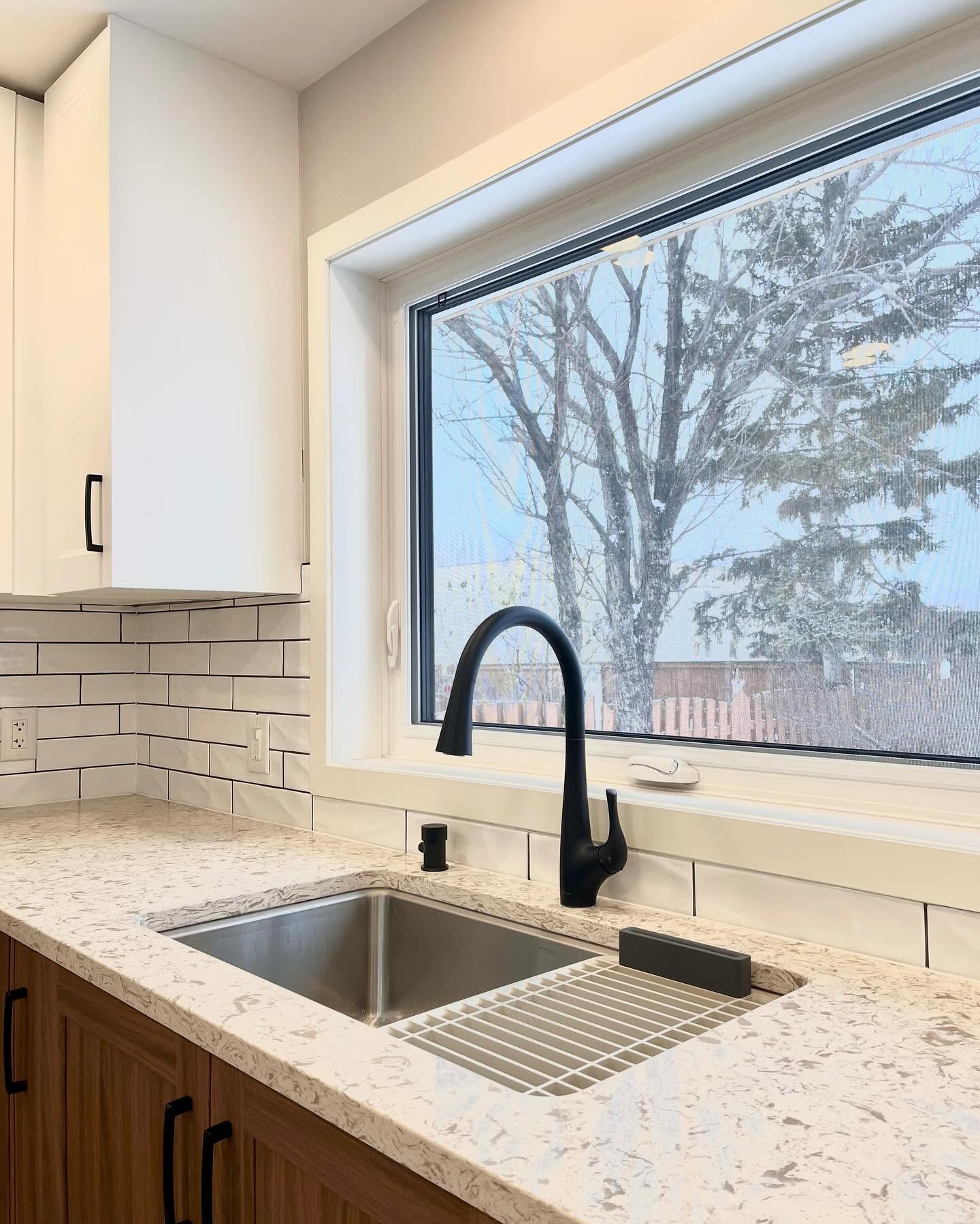 Finished Project Hydrangea sink wall with a black faucet, light stone counter, and a black-framed window